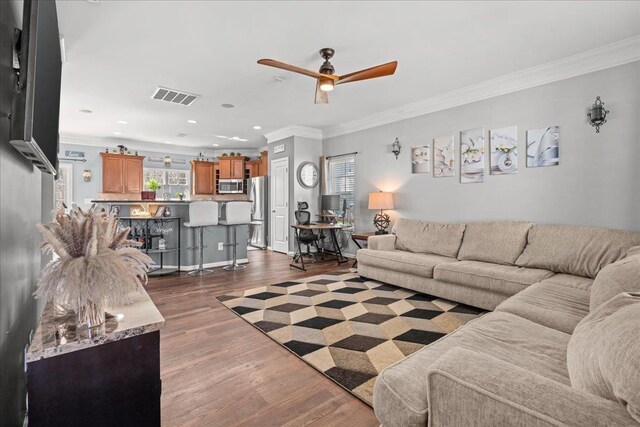 living area with dark wood-type flooring, crown molding, visible vents, and a ceiling fan