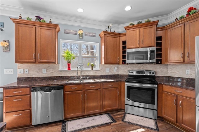 kitchen featuring crown molding, wood finished floors, appliances with stainless steel finishes, a sink, and brown cabinetry