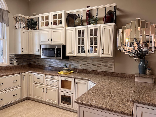 kitchen featuring glass insert cabinets, dark stone countertops, backsplash, and stainless steel microwave