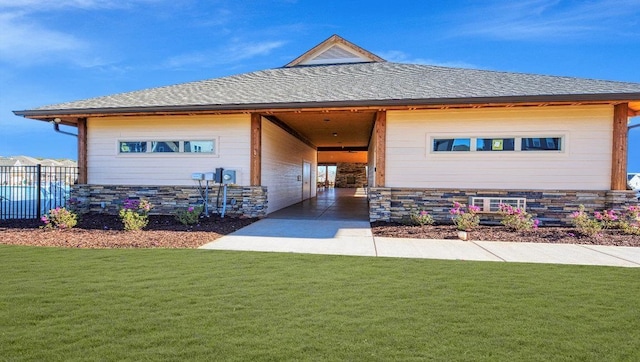 view of front of property featuring stone siding, a shingled roof, fence, and a front yard
