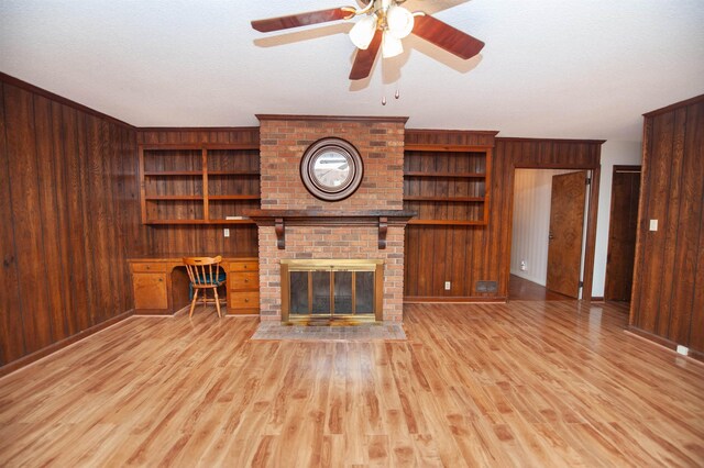 unfurnished living room with built in shelves, light wood-type flooring, a ceiling fan, and wooden walls
