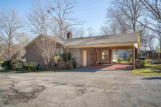 view of front facade with brick siding, an attached carport, driveway, and a chimney