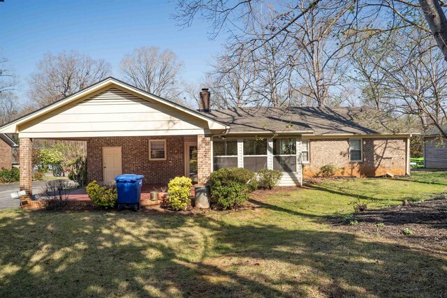 rear view of property with a chimney, brick siding, a carport, a lawn, and a patio area