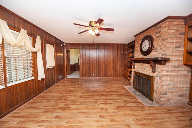 unfurnished living room featuring light wood-style flooring, a ceiling fan, wood walls, and a fireplace