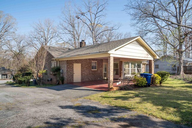 view of front facade featuring a chimney, brick siding, aphalt driveway, a front lawn, and a carport