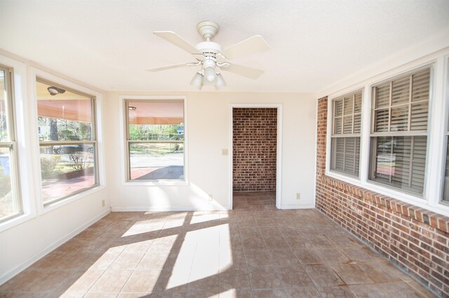 unfurnished sunroom with baseboards, ceiling fan, tile patterned flooring, and brick wall