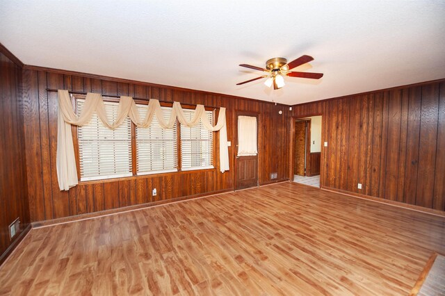 spare room with a ceiling fan, wood walls, baseboards, and light wood finished floors