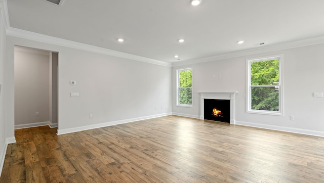 unfurnished living room with wood finished floors, ornamental molding, a warm lit fireplace, recessed lighting, and baseboards
