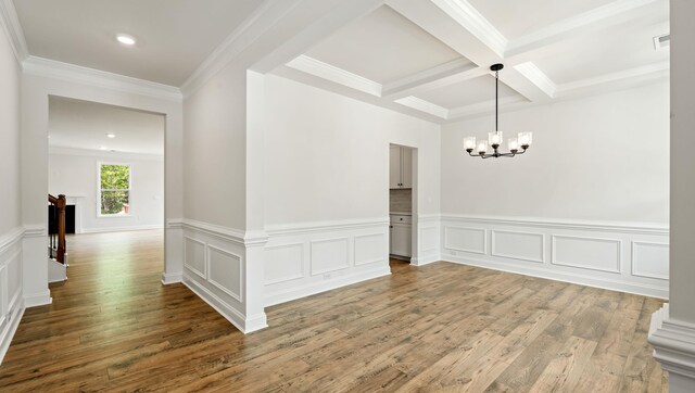 unfurnished dining area featuring a chandelier, beamed ceiling, wood finished floors, a wainscoted wall, and coffered ceiling