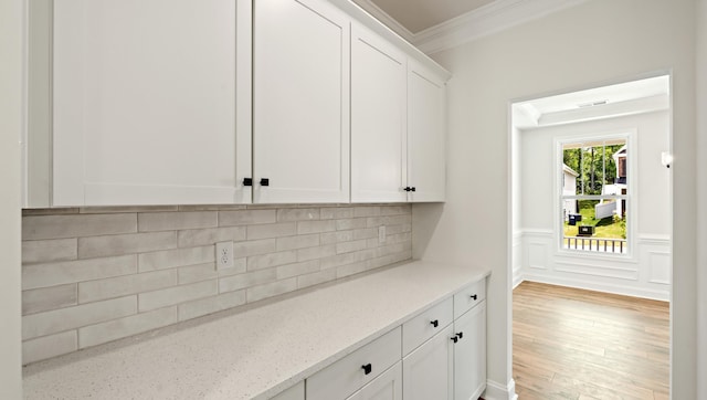 kitchen featuring crown molding, white cabinets, decorative backsplash, light stone counters, and light wood-style flooring