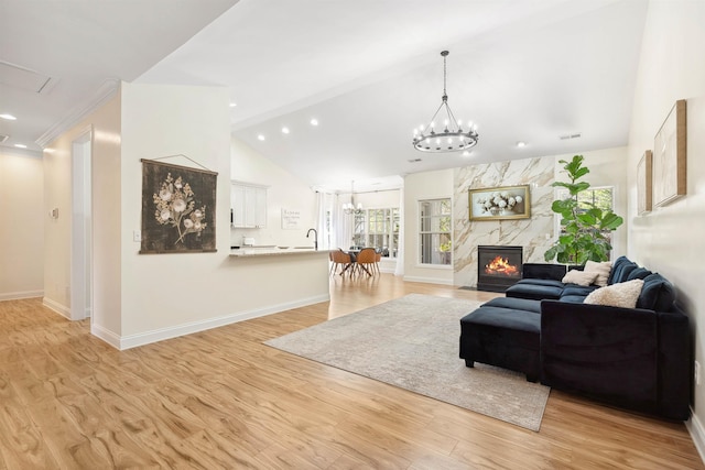 living area with baseboards, light wood-type flooring, lofted ceiling, and an inviting chandelier