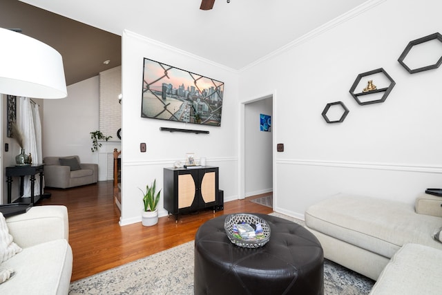 living area featuring a ceiling fan, crown molding, baseboards, and wood finished floors