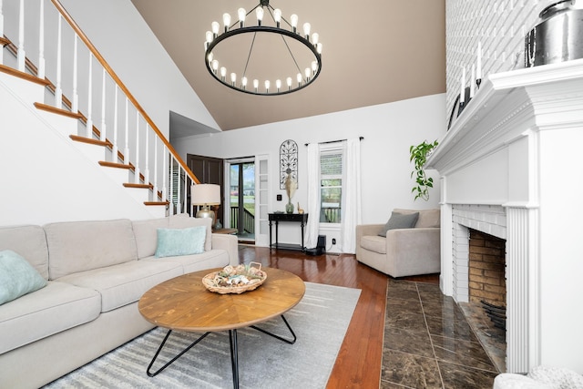 living area featuring stairway, high vaulted ceiling, a chandelier, a fireplace, and wood finished floors