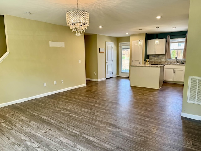 unfurnished living room featuring visible vents, a chandelier, dark wood-style flooring, a sink, and baseboards