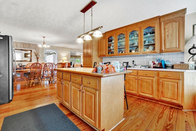 kitchen with light wood-type flooring, glass insert cabinets, light countertops, freestanding refrigerator, and backsplash