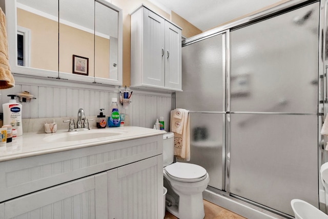 bathroom with toilet, vanity, a wainscoted wall, and a stall shower