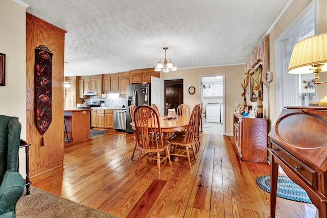 dining space with washer / dryer, light wood-style flooring, a textured ceiling, and an inviting chandelier