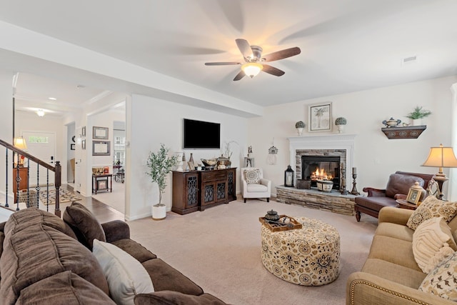 carpeted living room with visible vents, a ceiling fan, a stone fireplace, and stairway