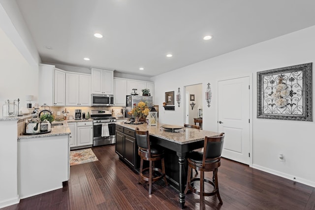 kitchen with dark wood finished floors, a center island, light stone counters, and appliances with stainless steel finishes