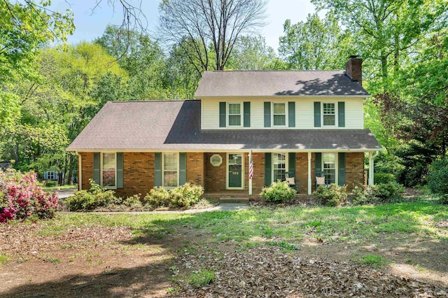 view of front of house featuring brick siding, a porch, and a chimney