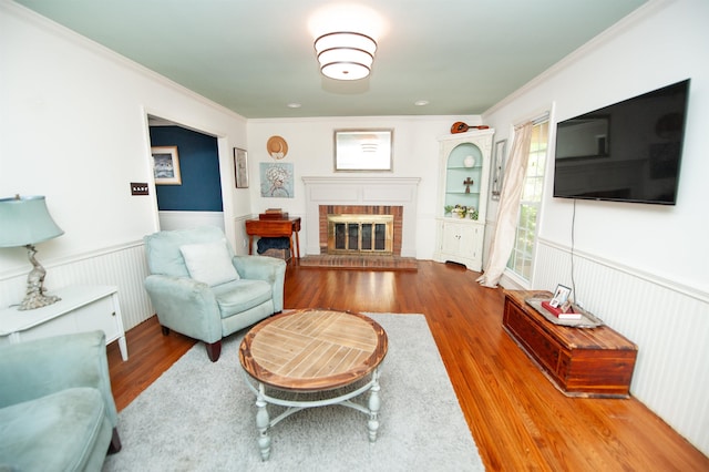 living room featuring wood finished floors, ornamental molding, a fireplace, and wainscoting