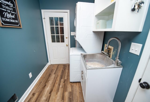 washroom featuring cabinet space, baseboards, stacked washing maching and dryer, and wood finished floors