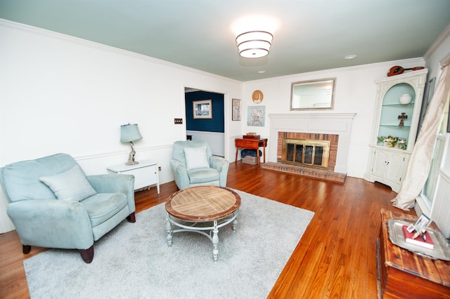 living area featuring a fireplace, ornamental molding, a wainscoted wall, and wood finished floors