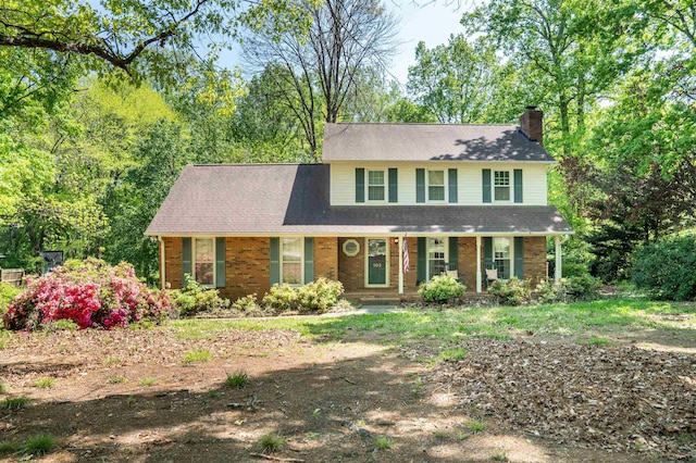 view of front of home featuring a chimney, covered porch, and brick siding
