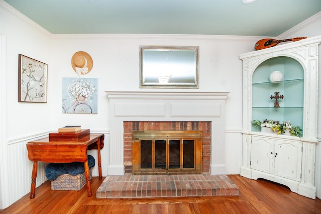 interior space featuring ornamental molding, a wainscoted wall, wood finished floors, and a brick fireplace