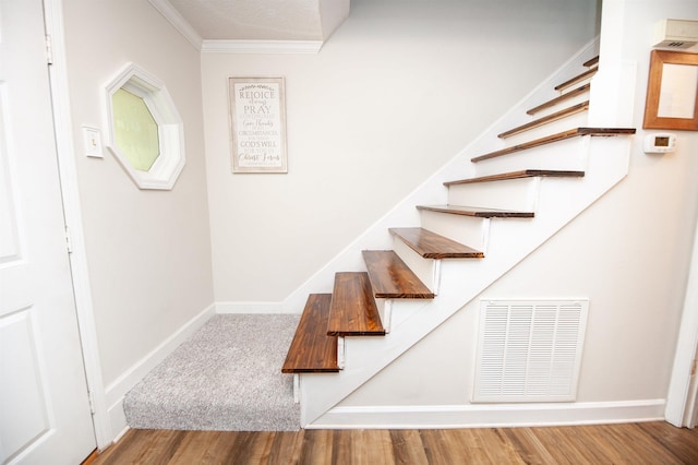 staircase featuring wood finished floors, baseboards, ornamental molding, and visible vents