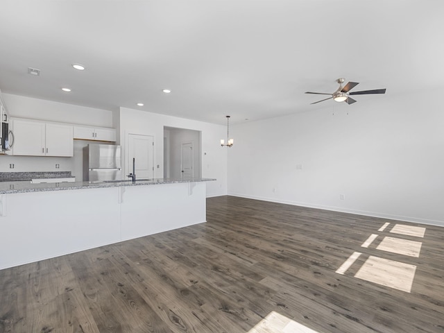 unfurnished living room with ceiling fan with notable chandelier, baseboards, recessed lighting, and dark wood finished floors