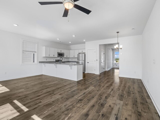 kitchen featuring stainless steel appliances, a peninsula, a sink, dark wood-style flooring, and a breakfast bar