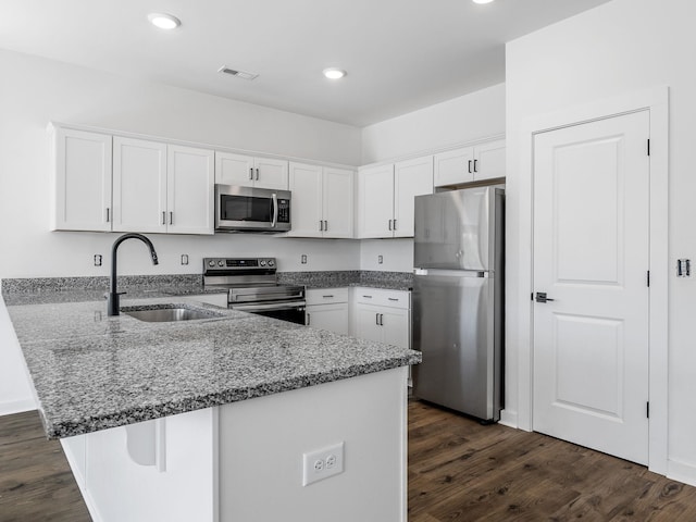 kitchen featuring white cabinets, a sink, stone counters, a peninsula, and appliances with stainless steel finishes