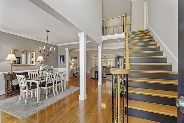 interior space with wood finished floors, a notable chandelier, ornate columns, and crown molding