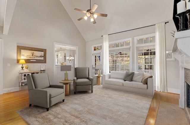 living area featuring a fireplace with flush hearth, light wood-style flooring, high vaulted ceiling, and ceiling fan with notable chandelier