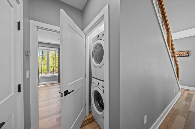 laundry area featuring stacked washer and clothes dryer, wood finished floors, baseboards, and laundry area