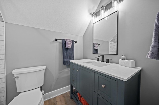 bathroom featuring toilet, wood finished floors, a textured ceiling, vanity, and lofted ceiling
