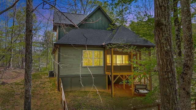 rear view of property featuring central AC unit and roof with shingles