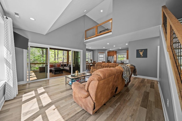 living area featuring high vaulted ceiling, plenty of natural light, visible vents, and light wood-type flooring