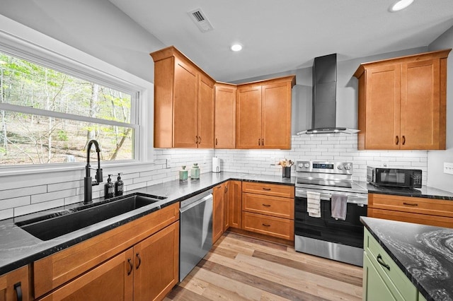 kitchen with light wood finished floors, visible vents, a sink, wall chimney exhaust hood, and appliances with stainless steel finishes