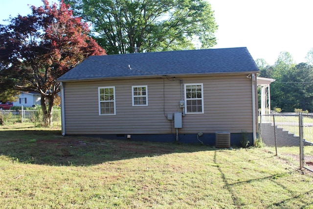 rear view of property with a yard, central AC unit, a shingled roof, and fence