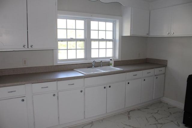 kitchen featuring marble finish floor, baseboards, white cabinetry, and a sink