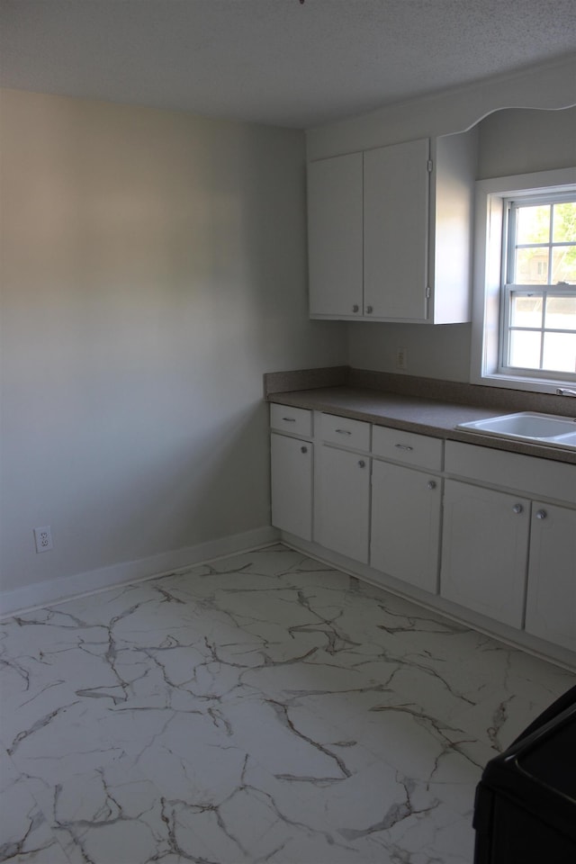 kitchen featuring marble finish floor, baseboards, white cabinetry, and a sink
