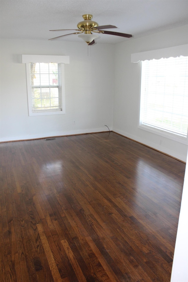 spare room with baseboards, visible vents, ceiling fan, and dark wood-style flooring