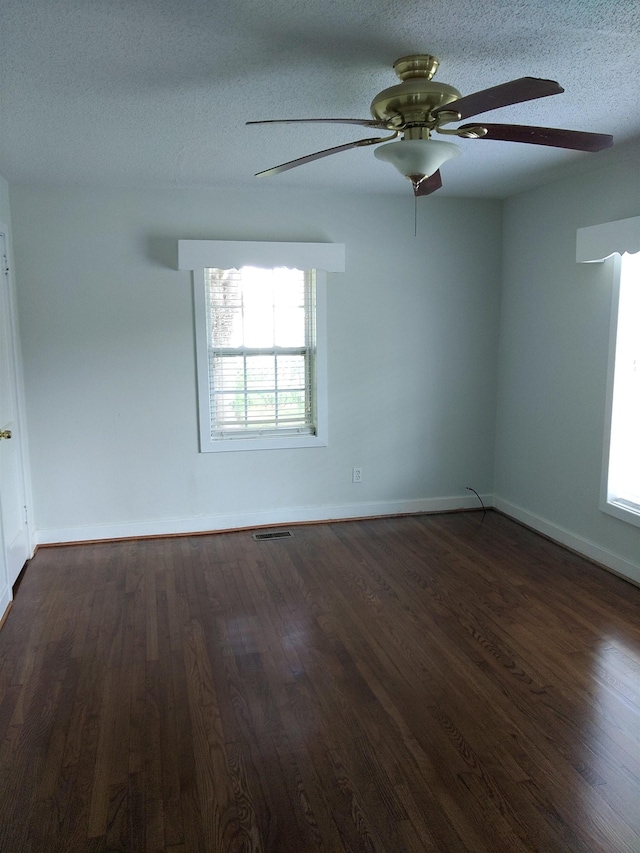 spare room featuring visible vents, a ceiling fan, baseboards, a textured ceiling, and dark wood-style flooring