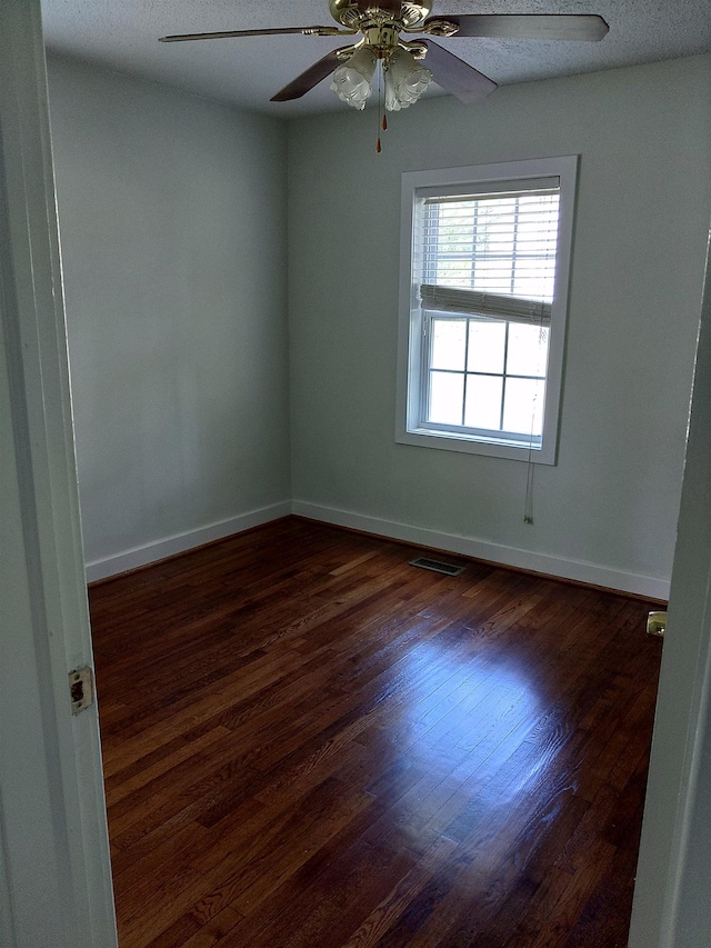 spare room with baseboards, visible vents, dark wood-type flooring, and ceiling fan