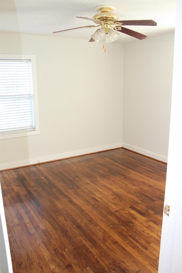 empty room featuring baseboards, a ceiling fan, and dark wood-style floors