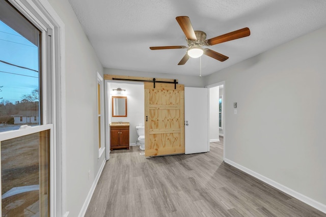 unfurnished bedroom with connected bathroom, a barn door, baseboards, and wood finished floors