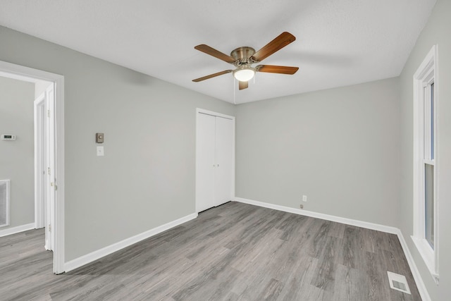 unfurnished bedroom featuring baseboards, wood finished floors, visible vents, and a closet