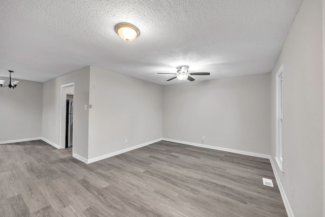 spare room featuring ceiling fan with notable chandelier, baseboards, wood finished floors, and visible vents
